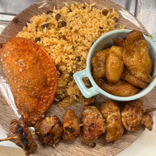 Mima's Cuban Cafe meal with rice, empanada, plantains, and chicken skewers on a wooden plate.