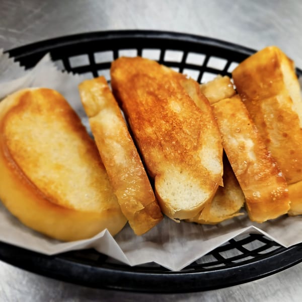 Golden brown, toasted Cuban bread slices in a black basket lined with white paper.