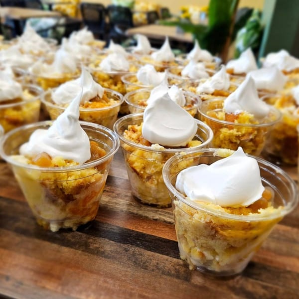 Rows of individual Cuban desserts in clear cups, topped with white meringue, on a wooden table.