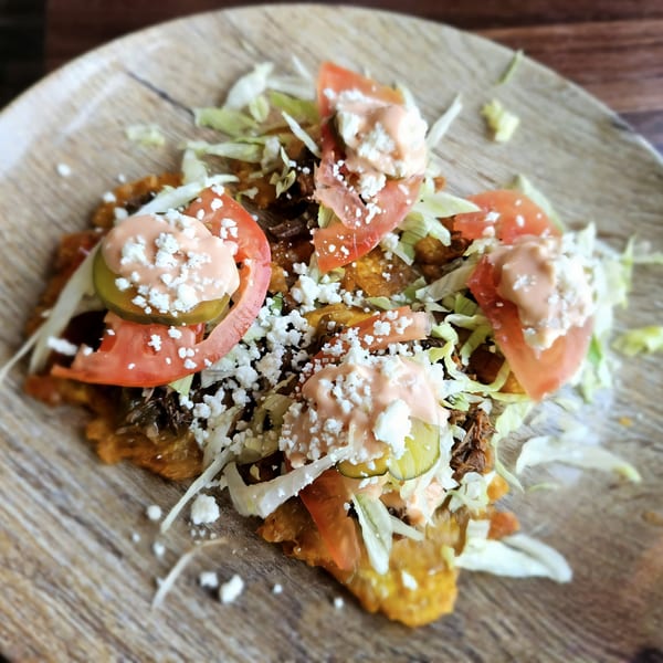 Cuban tostones topped with shredded beef, lettuce, tomatoes, cheese, and a creamy sauce.